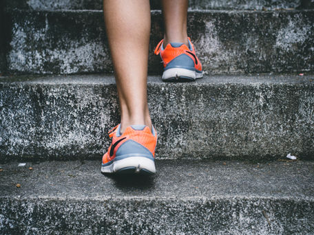 Person wearing bright orange and gray sneakers walking up concrete steps. The background is a textured gray, creating an active mood.