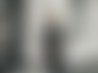 Man wearing a taupe wool coat, black sweater, and flat cap walking on a city street — modern minimalist style representing quiet luxury gifts for him.