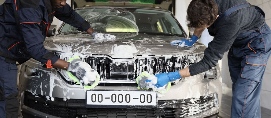Two detailers soaping and washing a car side by side in the bay — mobile detailing crew management app.