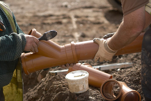 Hands applying adhesive to orange PVC drain pipe fittings