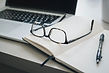 Desk with computer, open notebook, writing utensil and glasses