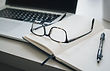 Desk with computer, open notebook, writing utensil and glasses