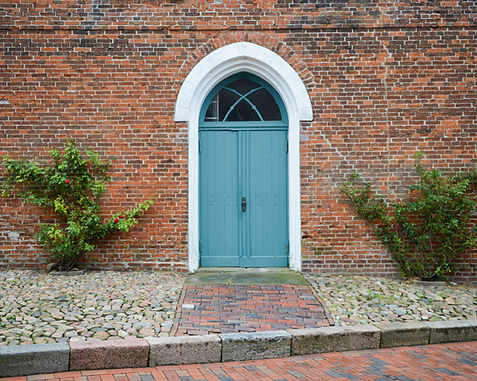 Arched blue door in a red brick wall with white trim and green plants