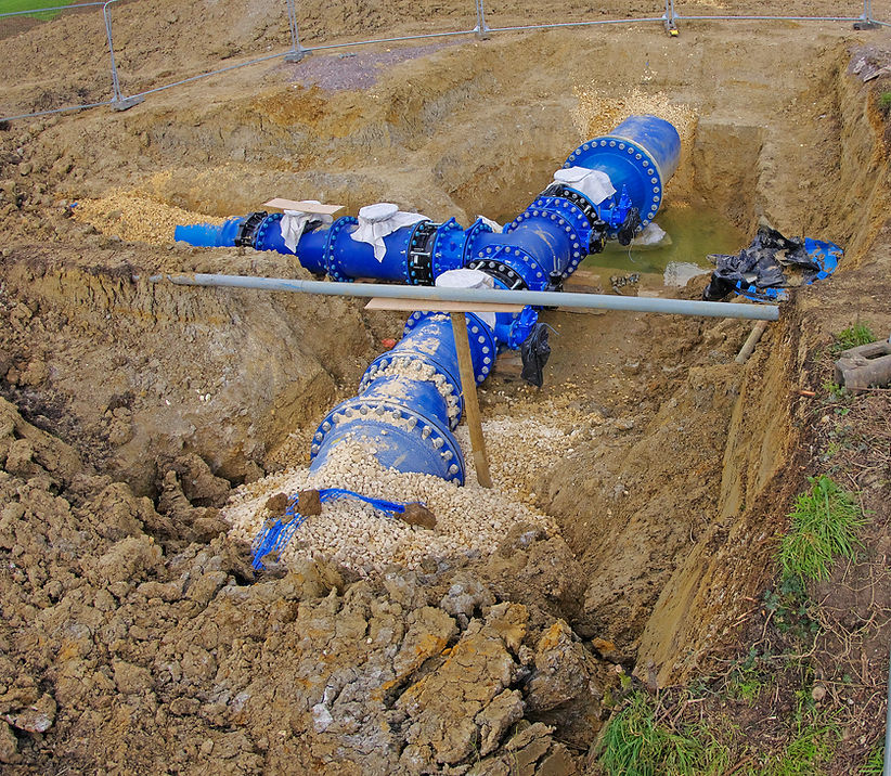 Heavy industrial water pipe valves and utility pipeline junctions installed deep inside an excavated earth trench