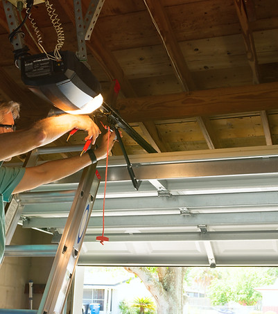 Professional automatic garage door opener repair service technician man working on a ladde
