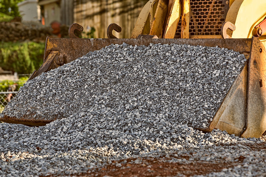 A bulldozer dumps a pile of gray gravel on the ground