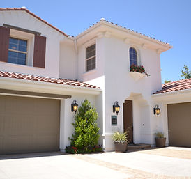Two-story white home from the driveway showing front of the house, brown garage doors, and wooden brown front door.
