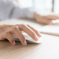 Hand using a white mouse on a wooden desk, with another hand typing on a keyboard. Soft lighting creates a calm, focused atmosphere.