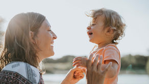 A mother and child outside, facing each other and smiling.