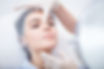 A woman in a medical cap lies back as a gloved hand examines her nose