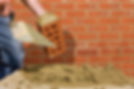 Close up of bricklayer applying mortar to brick with trowel in front of wall