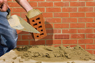 Close up of bricklayer applying mortar to brick with trowel in front of wall