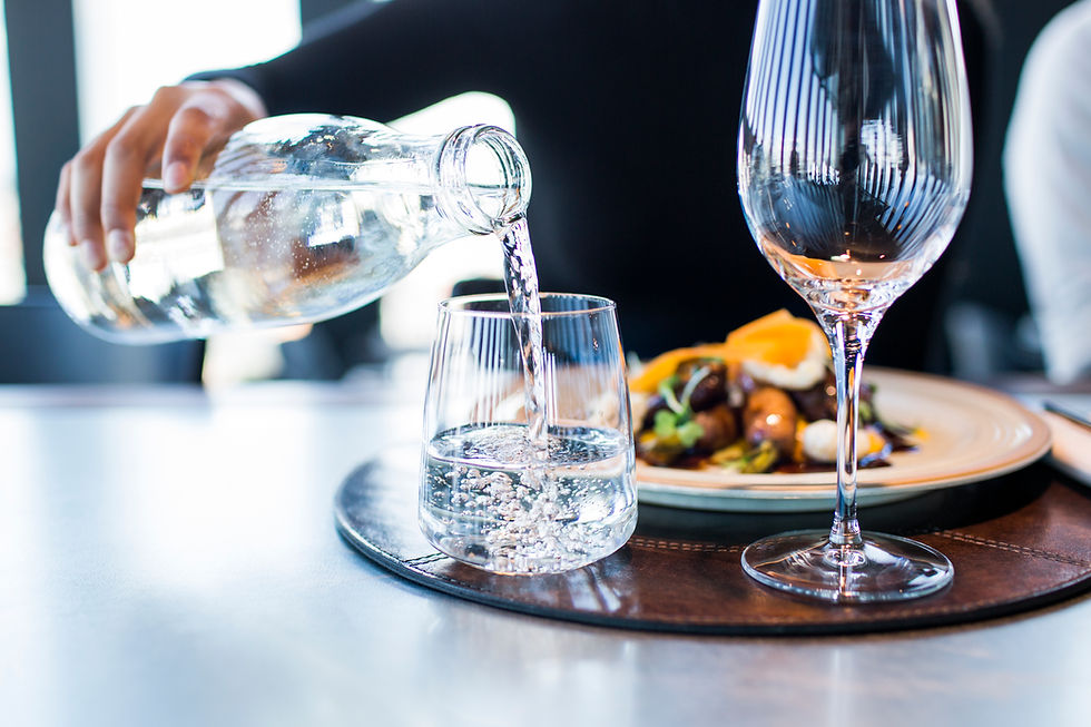 Server pouring water into a glass at a restaurant table with food