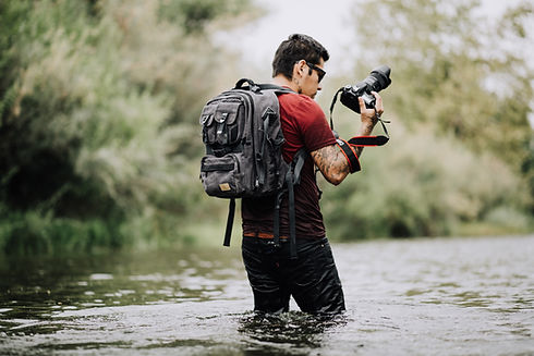 Photographer wading across a stream with camera in his hand