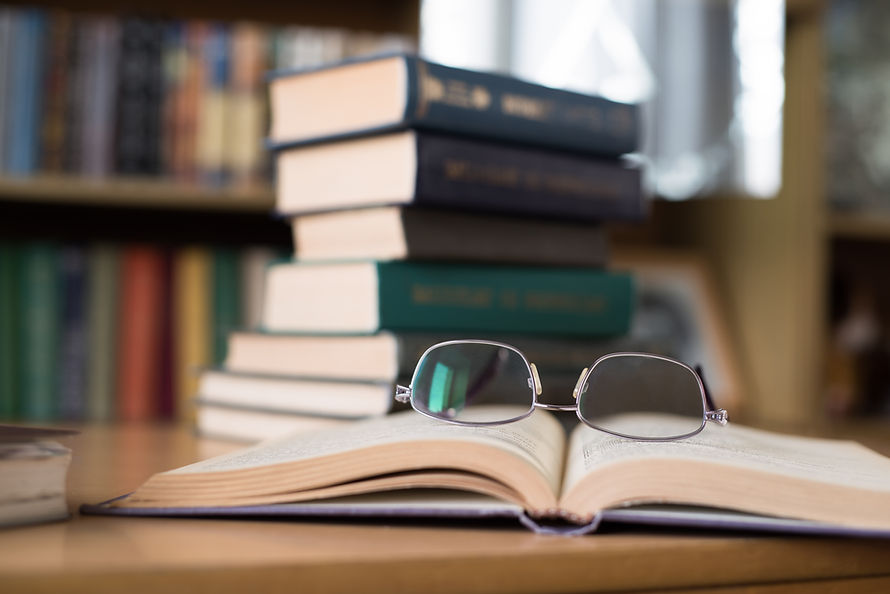 Open book with glasses on top and a stack of books in the background