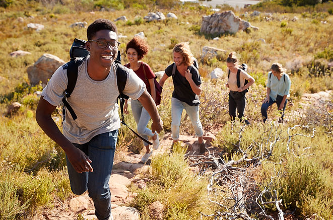 A group of five hikers walking up mountain. A young Black man leads the group, smiling.
