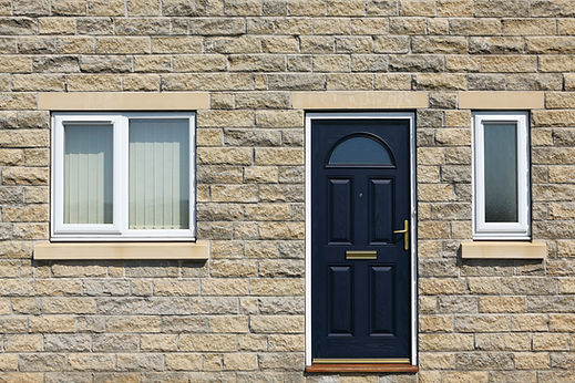 Dark blue front door and white double glazed windows set into a light stone brick cottage wall
