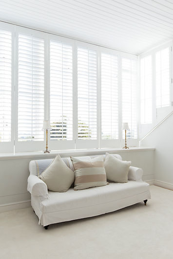 White interior window shutters installed above a neutral sofa in a bright room