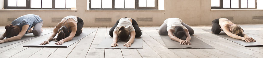 Window in background. People doing yoga on yoga mat. White floor. People wearing white shirts blank pants. white floor