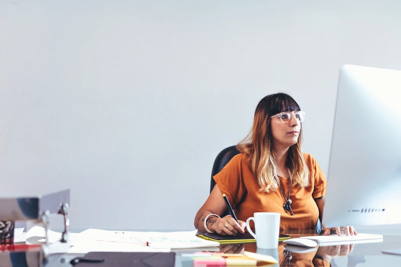 A woman sits in front of a desktop computer, focused and attentive to office work
