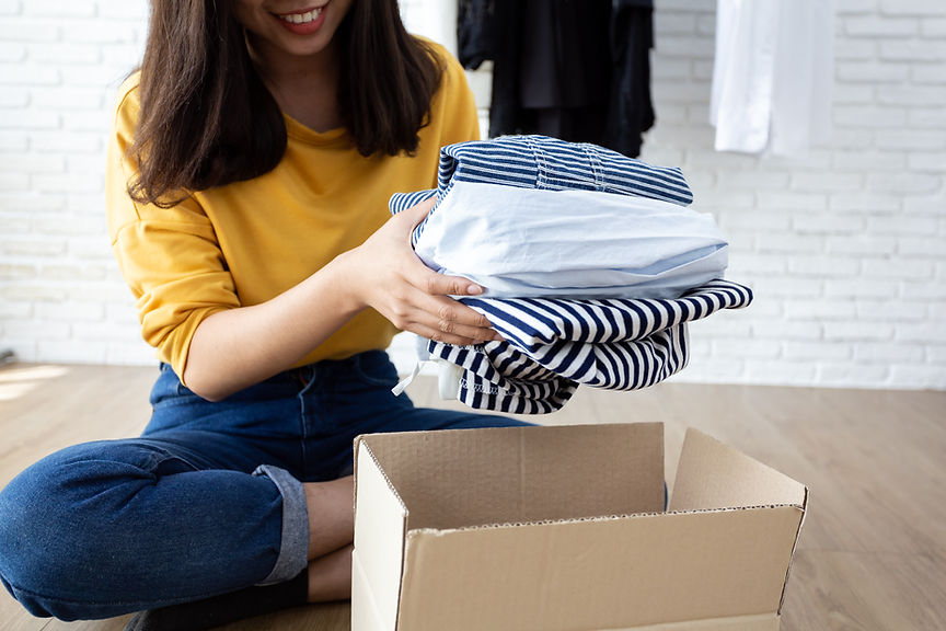 Mulher asiática sorridente colocando suas roupas em uma caixa