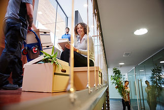 A woman sits on moving boxes, holding a tablet and smiling in a modern office