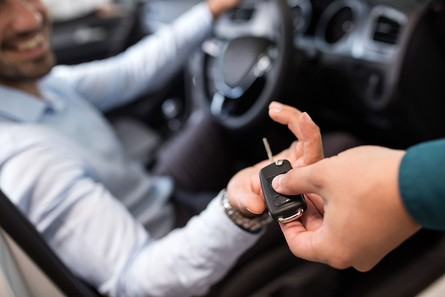 A man sitting in a car and receiving car keys from the dealer