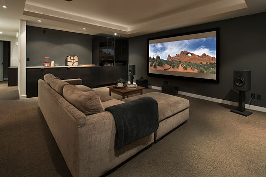 Home cinema room with a large projection screen, plush sectional sofa, and recessed dark cabinetry
