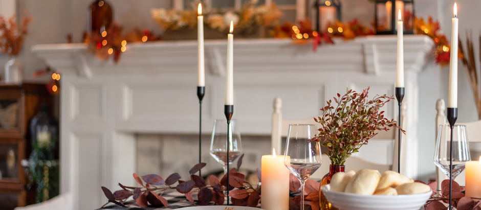 A cozy autumn table setting with candles, a floral centerpiece, and rolls in a bowl. Festive fall decor and warm colors in the background.