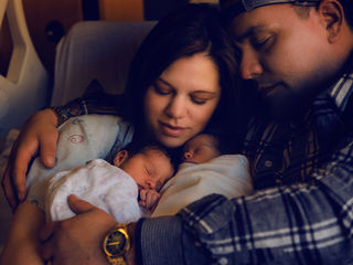 A mom and dad in a hospital bed with newborn twins wrapped in white blankets