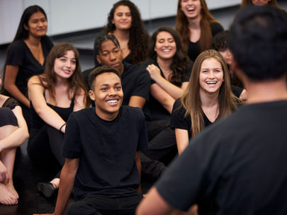 A group of youth adults sitting in a room. They are all wearing black t shirts laughing.