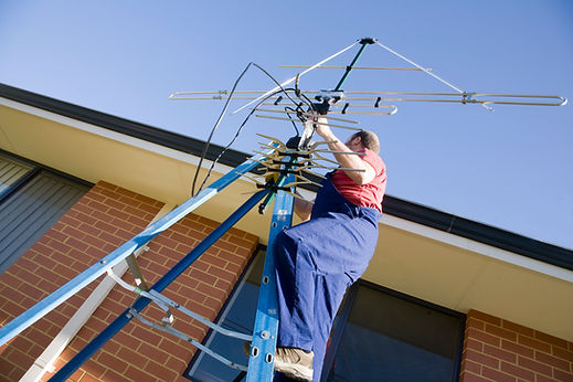 Installer aligning television aerial on ladder outside building