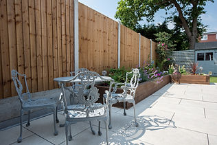 A general view of a back garden patio with white porcelain slabs, tiles, paving and wooden