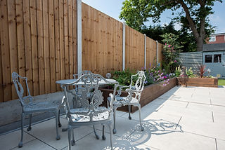 A general view of a back garden patio with white porcelain slabs, tiles, paving and wooden fencing