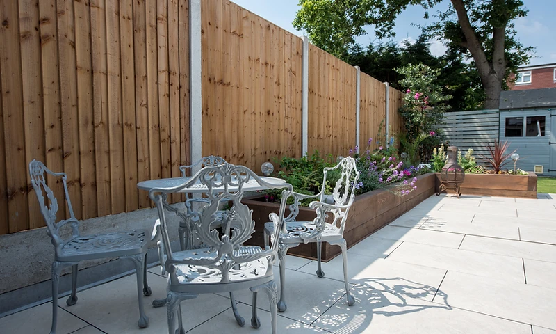 a back garden with porcelain patio slabs showing a table by the fence for people to socialise