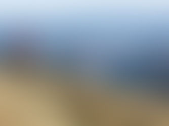 Two mountain bikers in red and blue ride along a grassy ridge above a vast mountain valley.