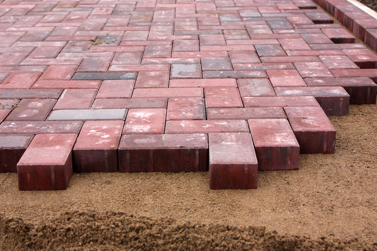 Paving bricks are arranged in a herringbone pattern on a sandy surface, showcasing a partially completed pathway