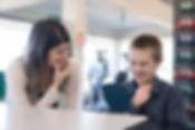 A woman and a young boy sit at a table, smiling and holding their chins