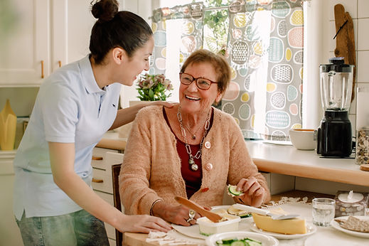 Cheerful senior woman talking with female caregiver in kitchen 
