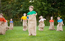 Eight boys and girls all races each other using potato sacks