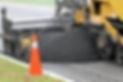 Rear quarter view of an asphalt paving machine at work, spreading asphalt for a new road s
