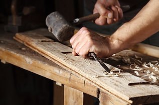 Hands using a wooden mallet and chisel to carve a decorative groove in a wooden plank