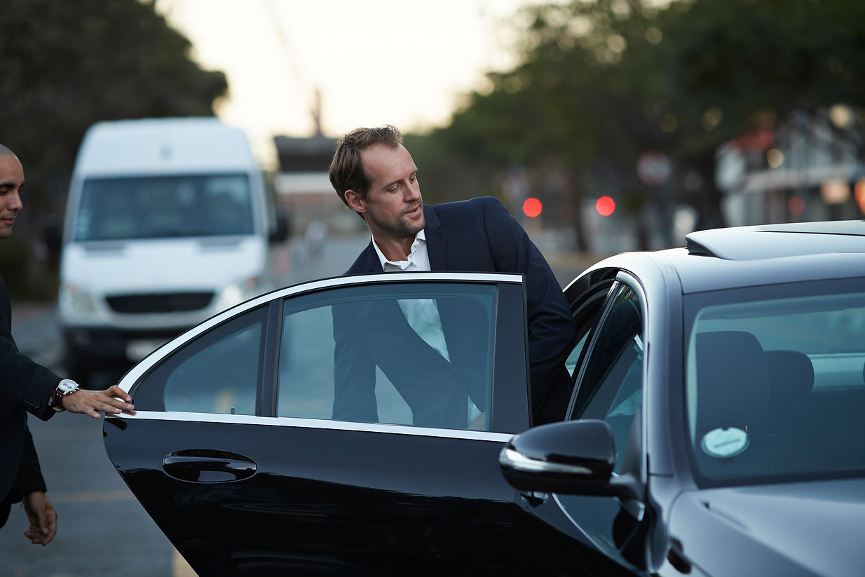 Two men in suits are entering a car, preparing for a journey together