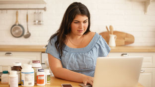 woman in kitchen with laptop and vitamin bottles