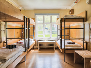 Bunk beds with rolled towels in a bright room, wooden furniture, large window showing a green yard and road outside. Cozy and tidy setting.
