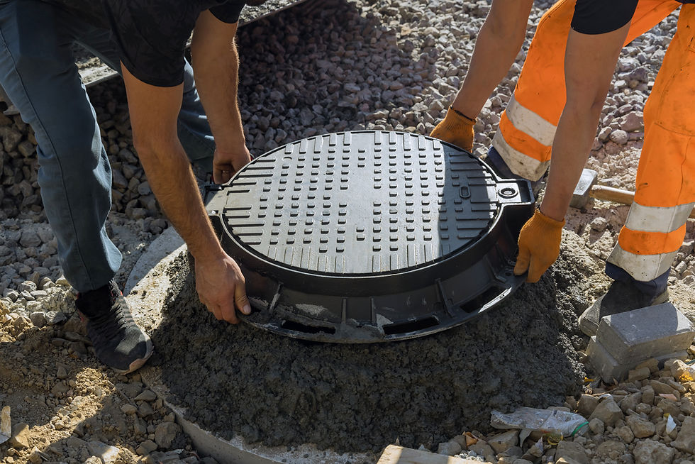 Two workers installing a heavy round manhole cover into concrete