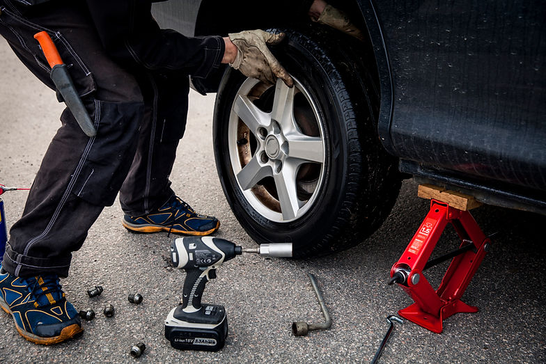 A person changes a car tire using a red jack and electric wrench