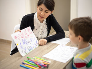 A young boy meeting with a childhood psychologist, holding a children's drawing.