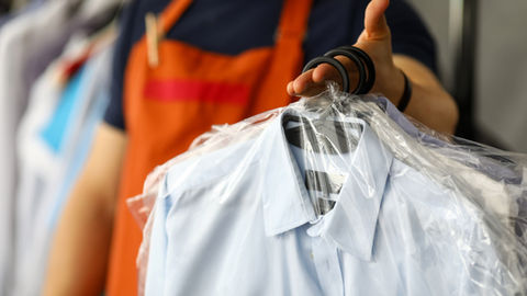 Employé en tablier orange tenant une chemise bleue sous plastique sur cintre, dans une boutique de vêtements.