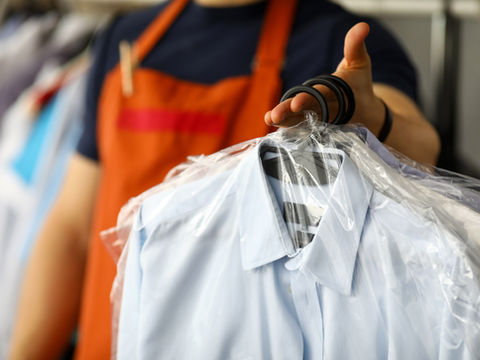 Employé en tablier orange tenant une chemise bleue sous plastique sur cintre, dans une boutique de vêtements.